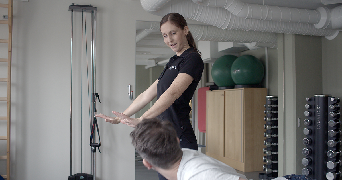 Kvinnlig fysioterapeut instruerar patient hur en rörelse ska utföras.