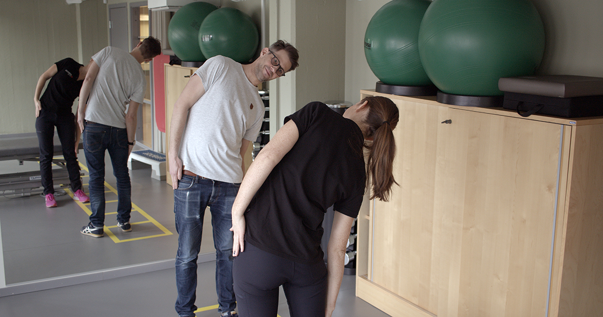 Kvinnlig fysioterapeut visar manlig patient hur en rörelse ska utföras.