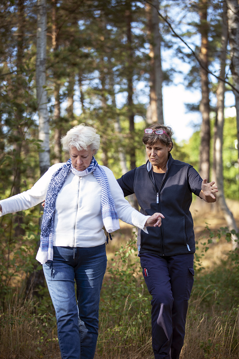 Äldre kvinna och kvinnlig fysioterapeut gör övningar utomhus.